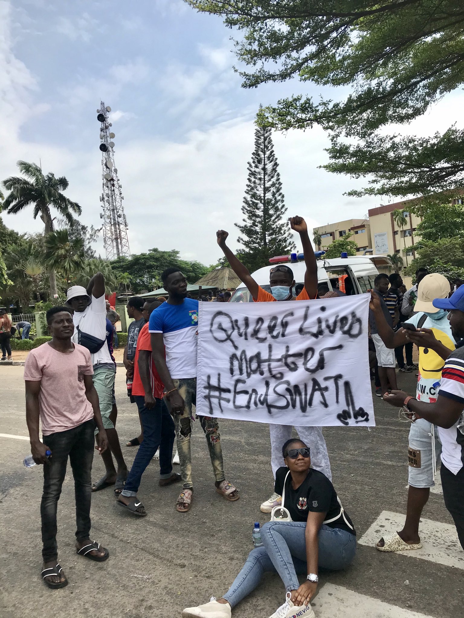Image shows Nigerian activists standing behind a sign with raised fists. The sign reads 'Queer lives Matter #EndSARS'