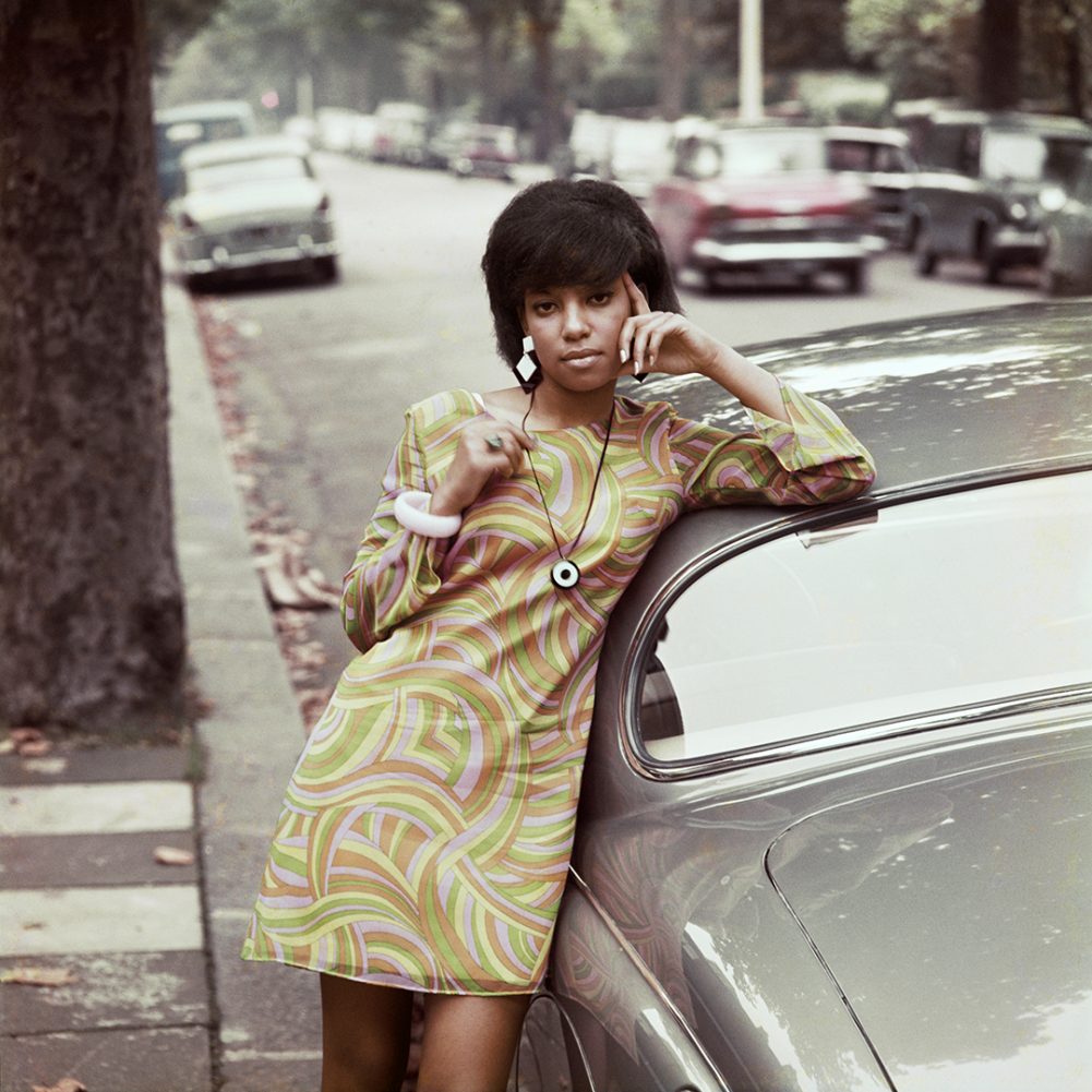 A woman leans on a car, shot by James Barnor