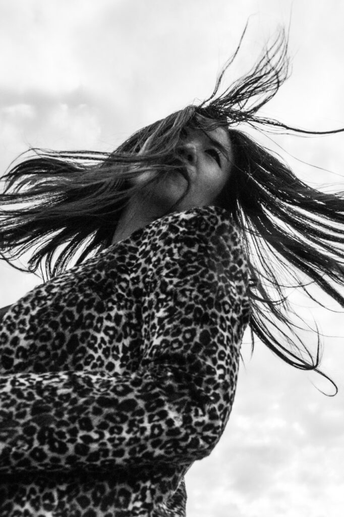 A black and white photograph of Nancy Whang. Her hair is swinging in the breeze and she's wearing leopard print.