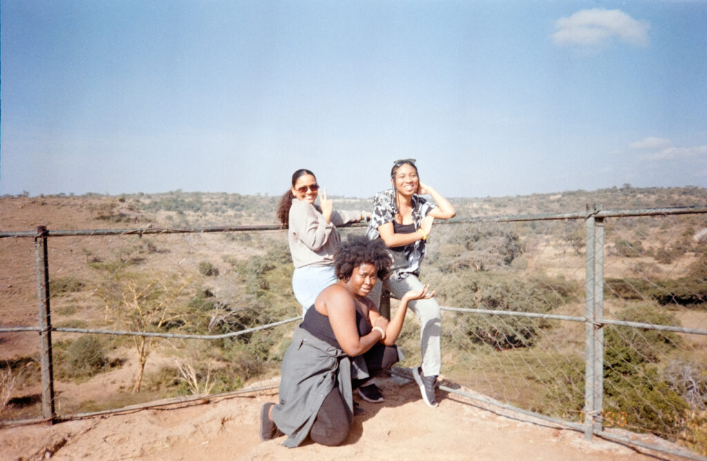 three people stand in front of Nairobi national park, posing for the camera. 