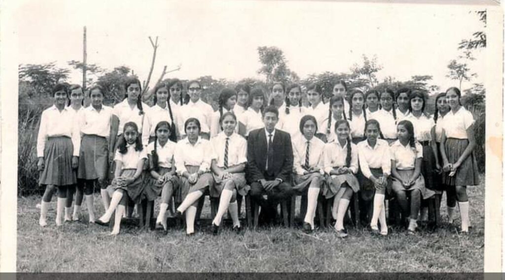 Landscape photo of a class of school pupils. In the middle there is Ramnik, as a teacher, surrounded by his pupils. They are sitting on the grass, while taller pupils behind are standing.
