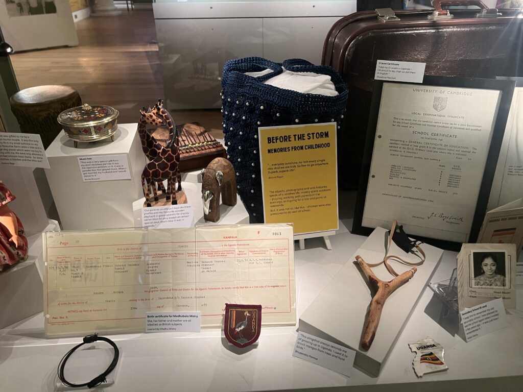 Landscape photo detailing a collection of items belonging to Ugandan Asians. These items include childhood memories such as a school certificate and badge, as well as childhood toys and small statues.