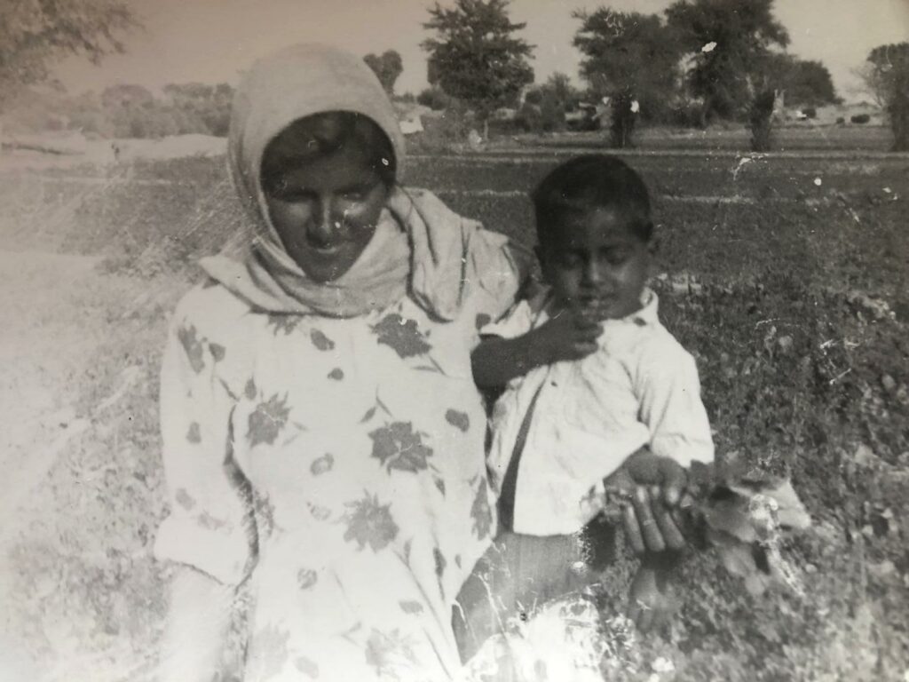 Picture of a woman wearing a tunic carrying a child. There is a field in the background. The picture is in black-and-white.