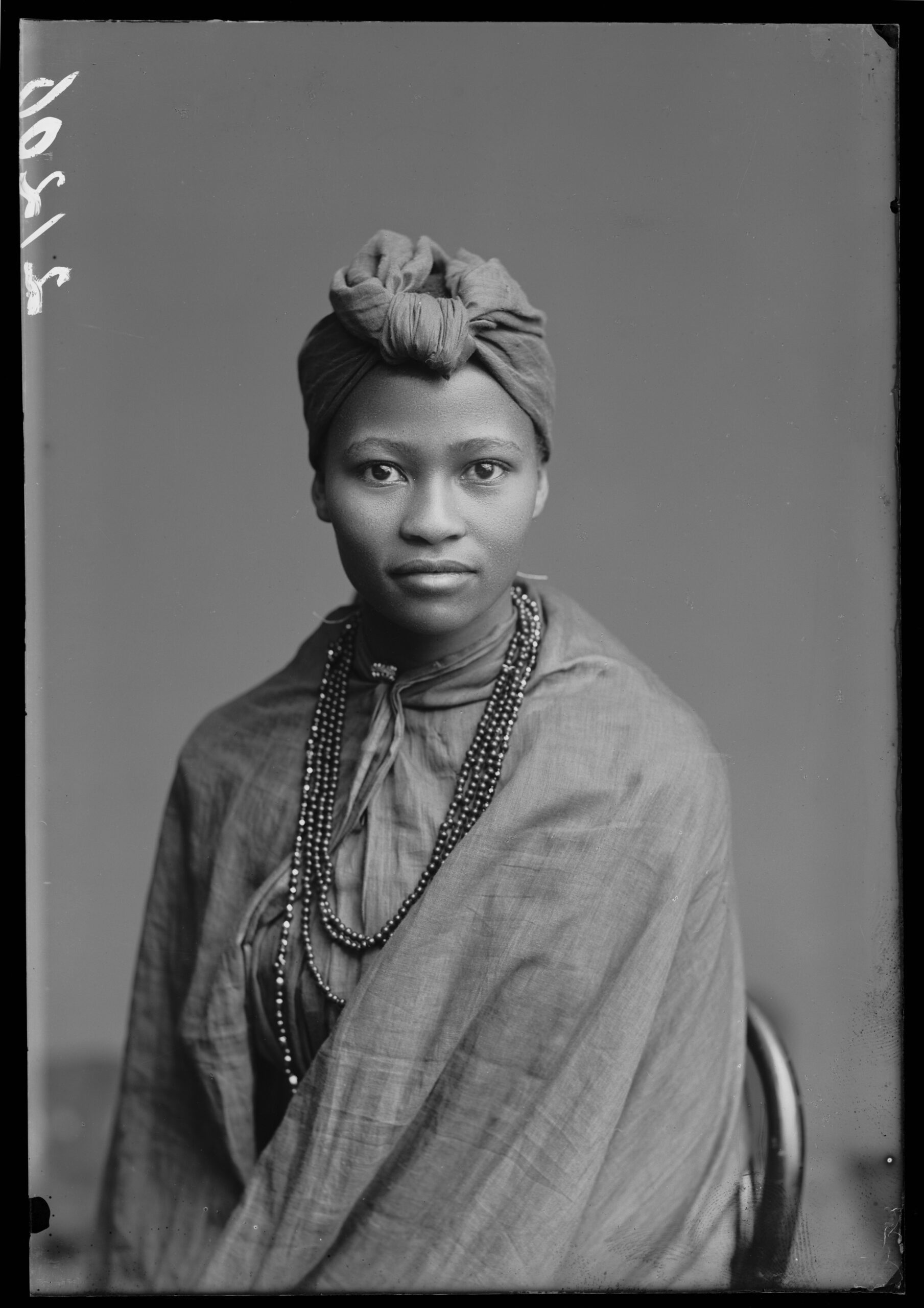 A black and white studio portrait of a woman seated looking at the camera. She is wrapped in soft cloths