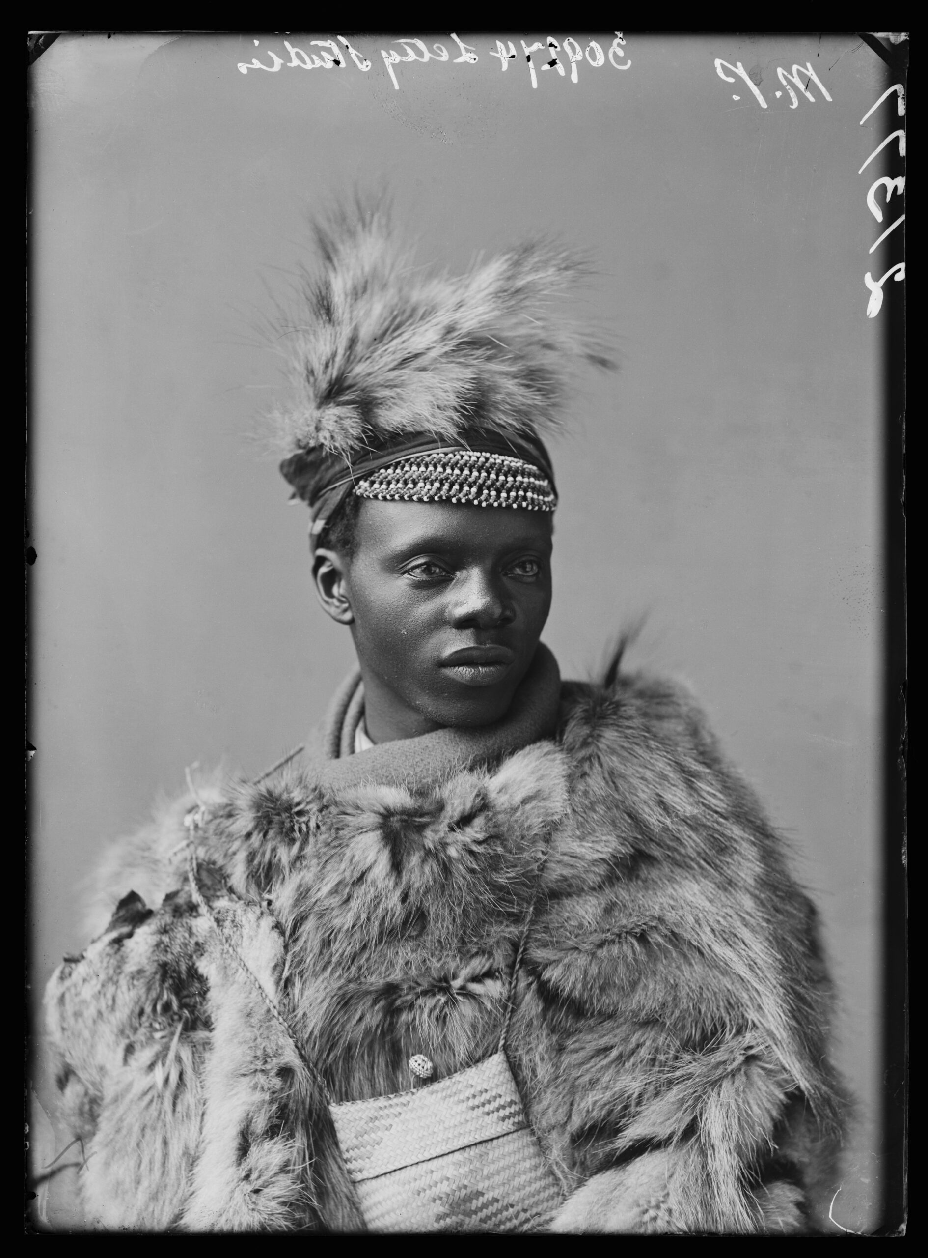 A studio portrait in black and white of a man wearing traditional dress, looking off to the left