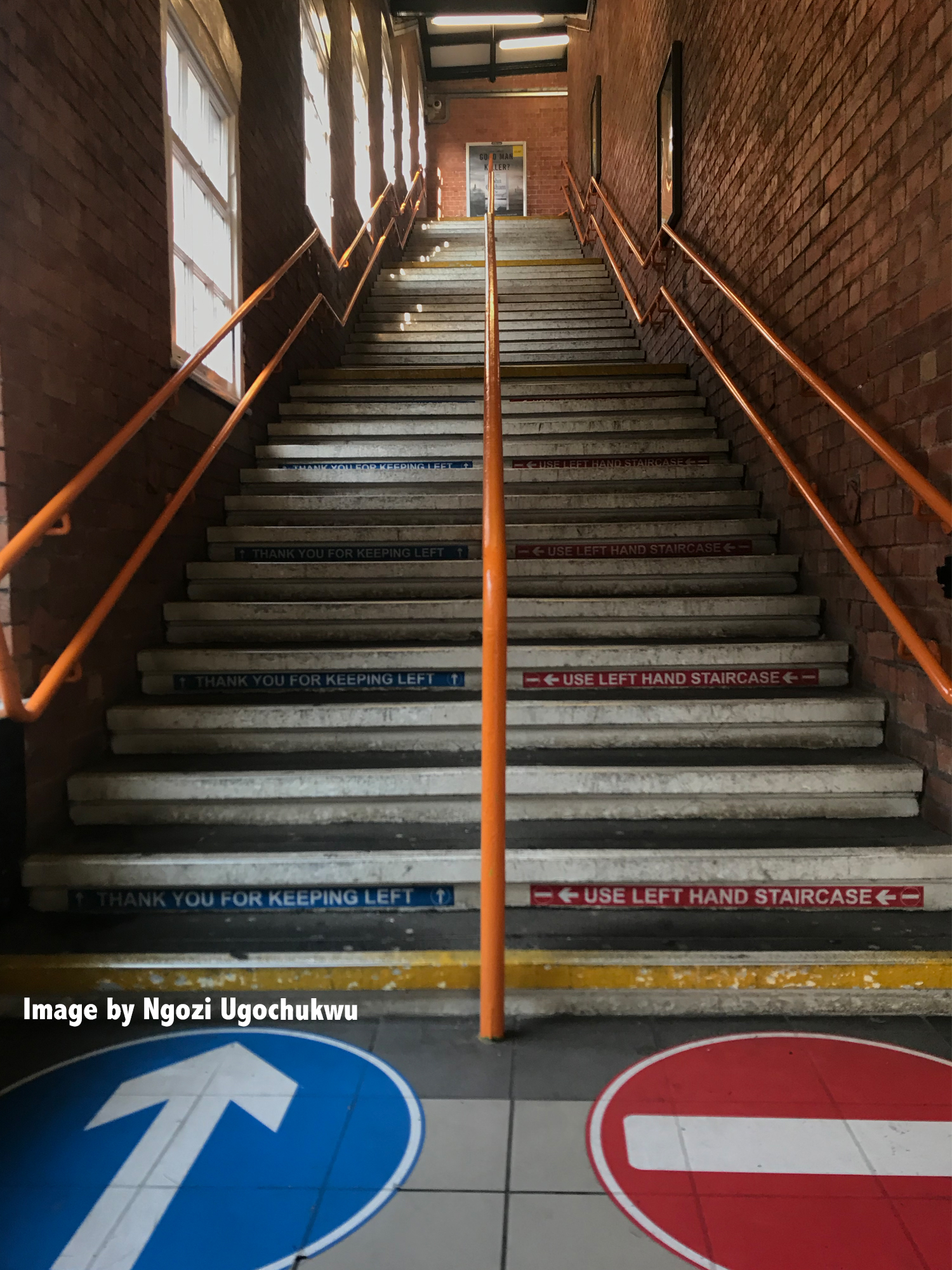 A view from the ground of grey concrete stairs looking upward with orange handrails