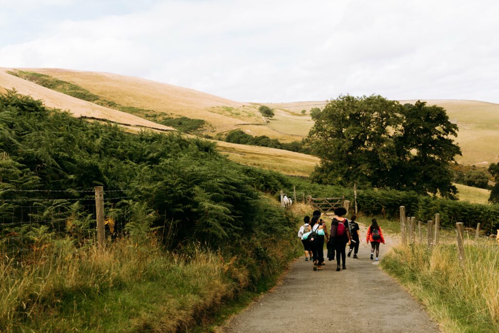 A group of people walk along a path with hills and trees in the background