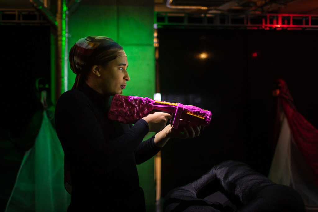 A photograph of Danielle from a profile view. She is holding a pink object that looks like a video game gun