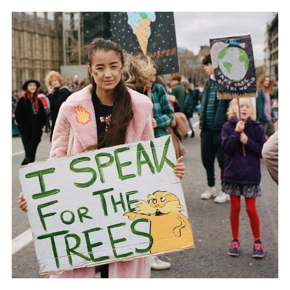 An image of Celina at a protest in London, holding a sign that says 'I speak for the trees'