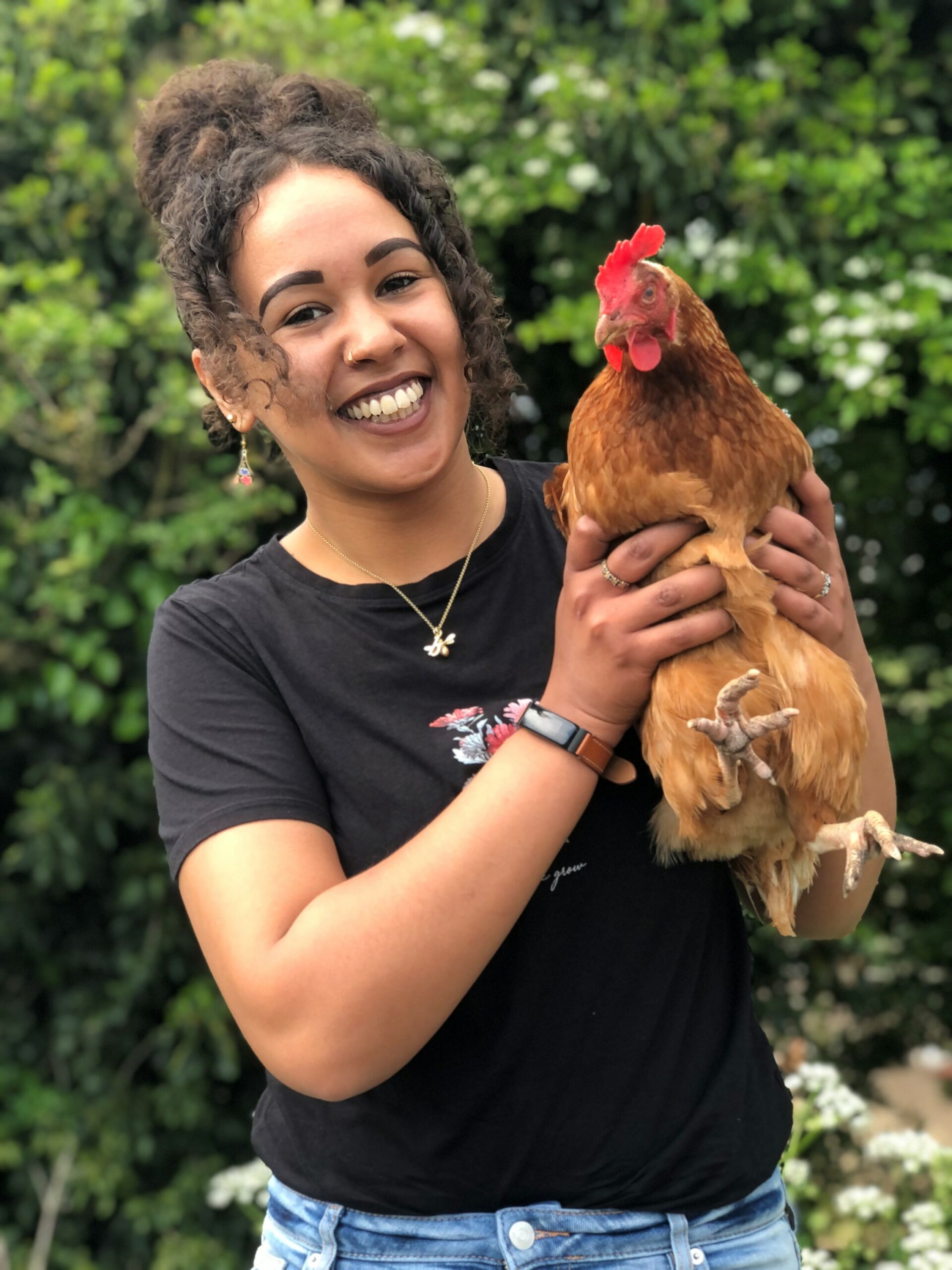 An image of Bushra holding a chicken, smiling and looking into the camera 