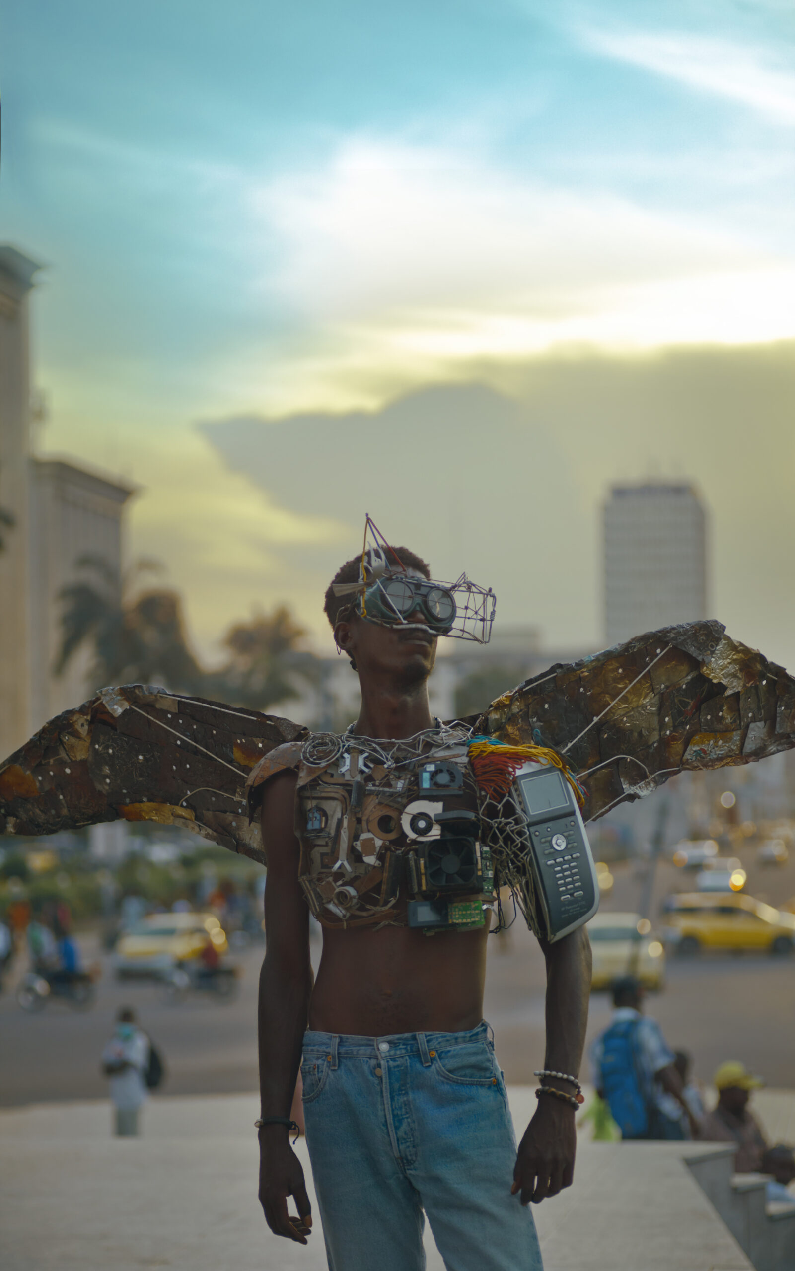 Man poses with wings made out of disused metal and electronics. 
