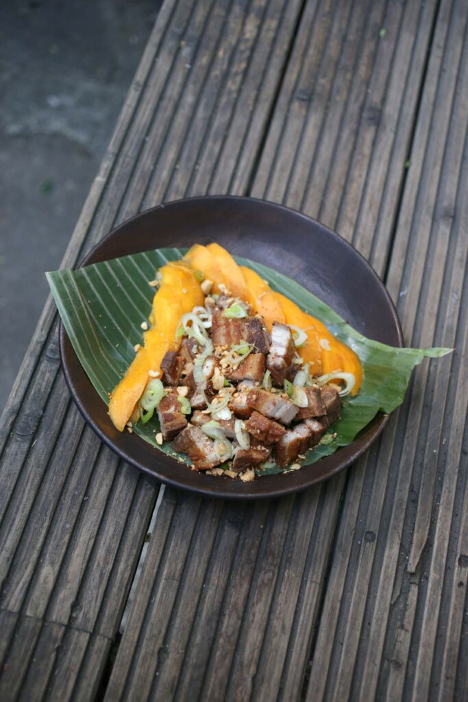 A photograph of a bowl of food from above. It is crispy pork belly with mango