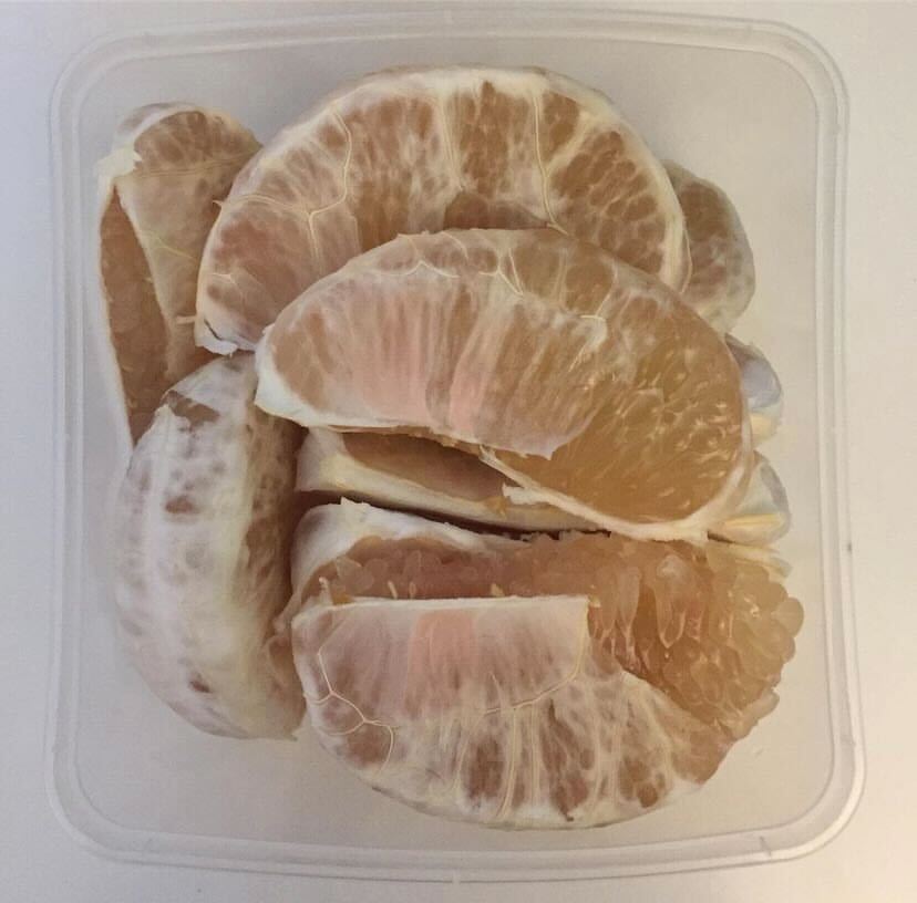 A photograph of cut pomelo in a tupperware container