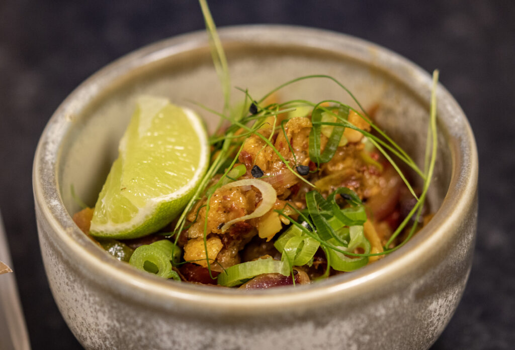 A photograph of a grey ceramic bowl with a slice of lime, fried food, chopped spring onion 