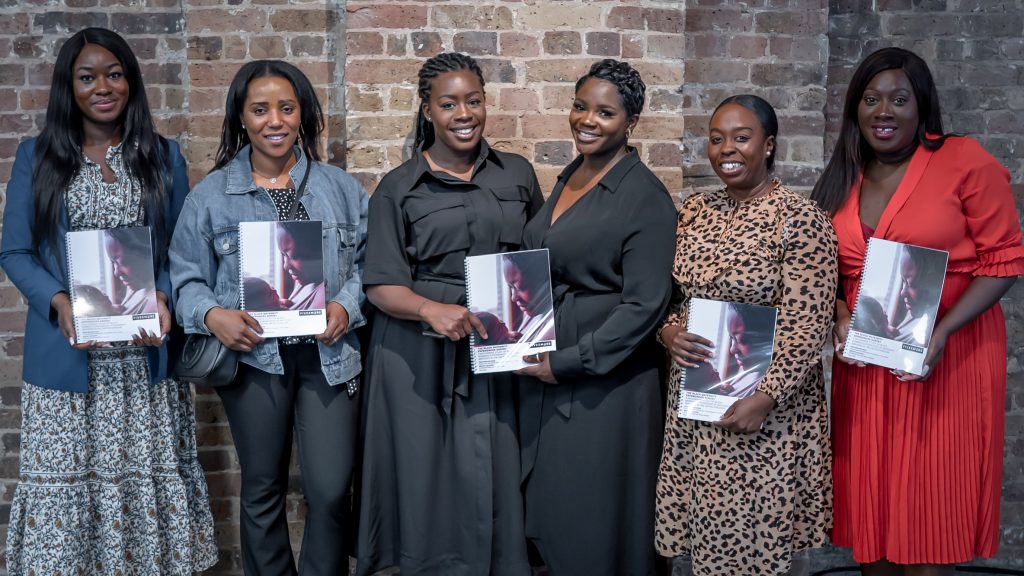 Six black women stand next to eachother, all smiling and each holding a folder.