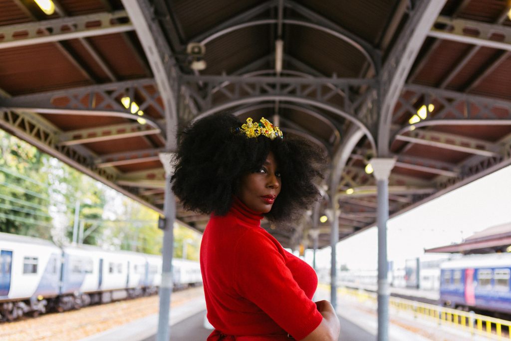 a photograph of a woman looking into the camera. she is wearing a red top and has a crown on top of her afro